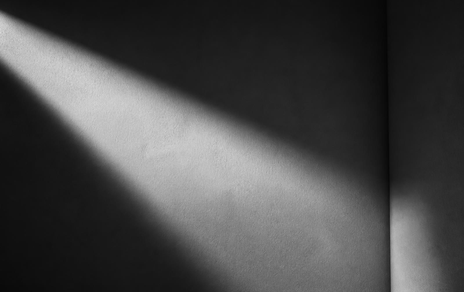 Feixe geométrico de luz sobre parede vazia, quase abstrato, em preto e branco
